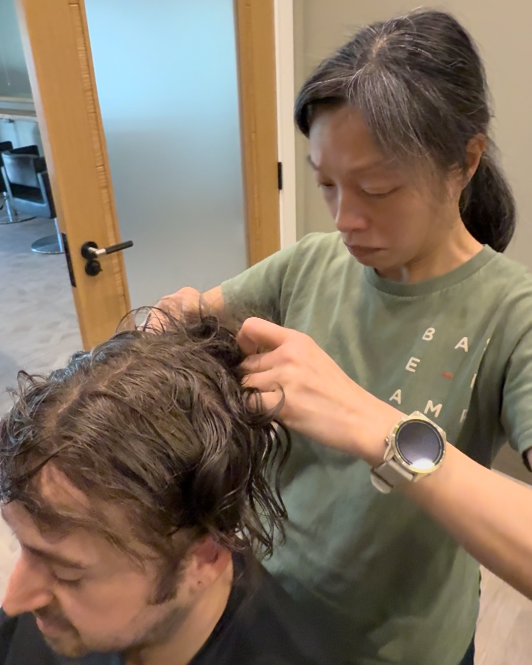 Stylist matching a hair system base to a client's natural hairline in a salon