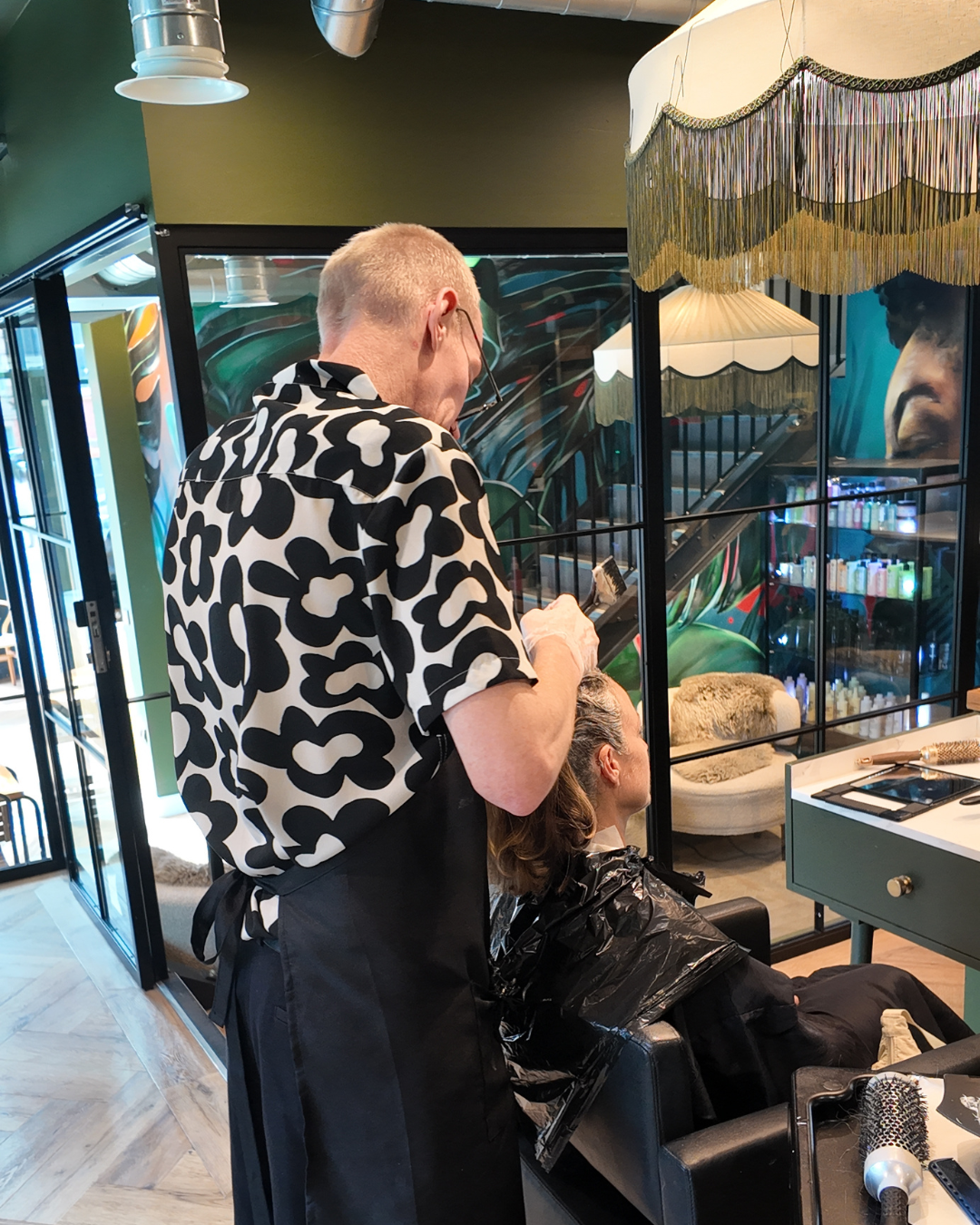Stylist applying colour to a blonde client's hair at a styling station