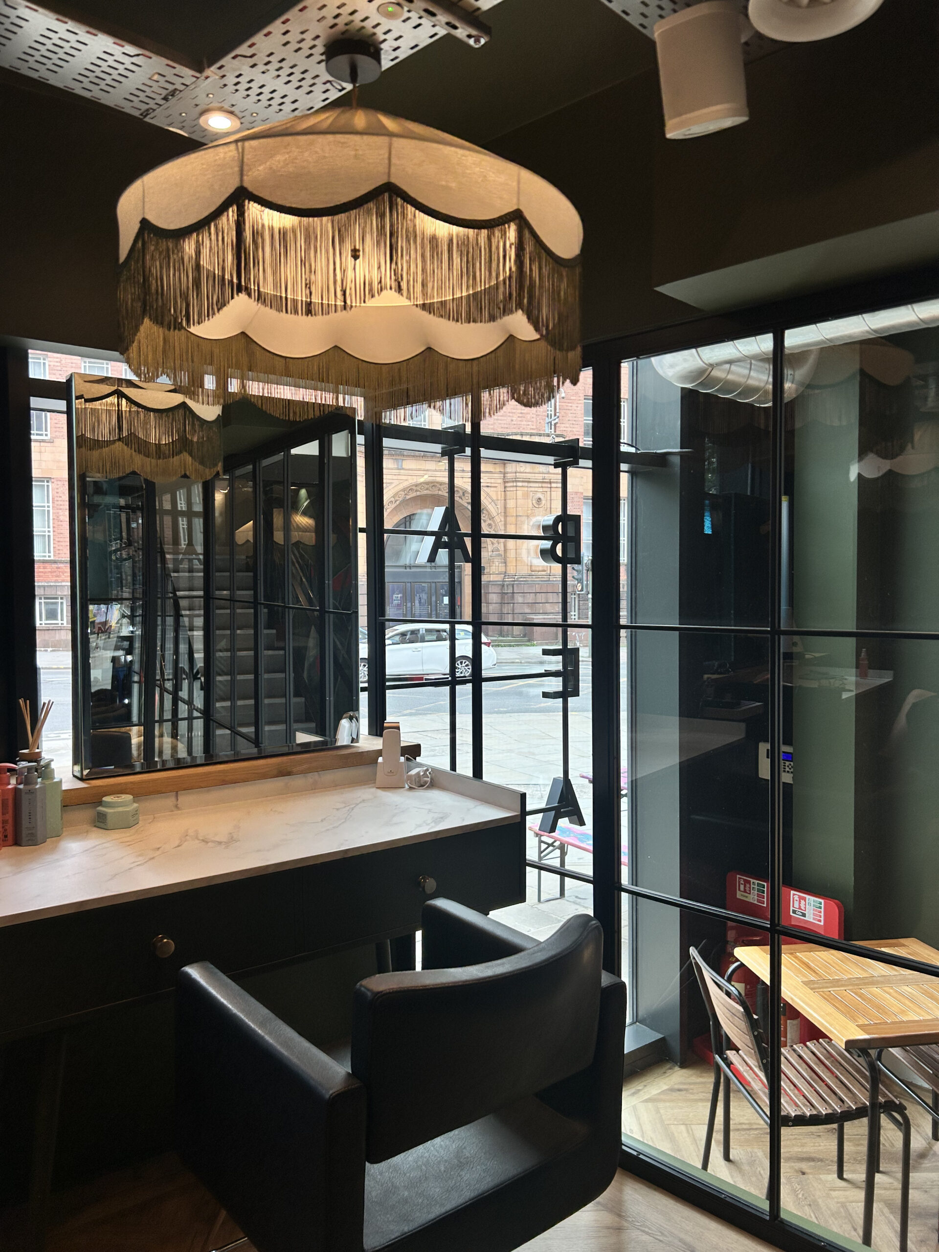 Styling station with a black chair and fringed lampshade at David Rozman hair salon in Manchester