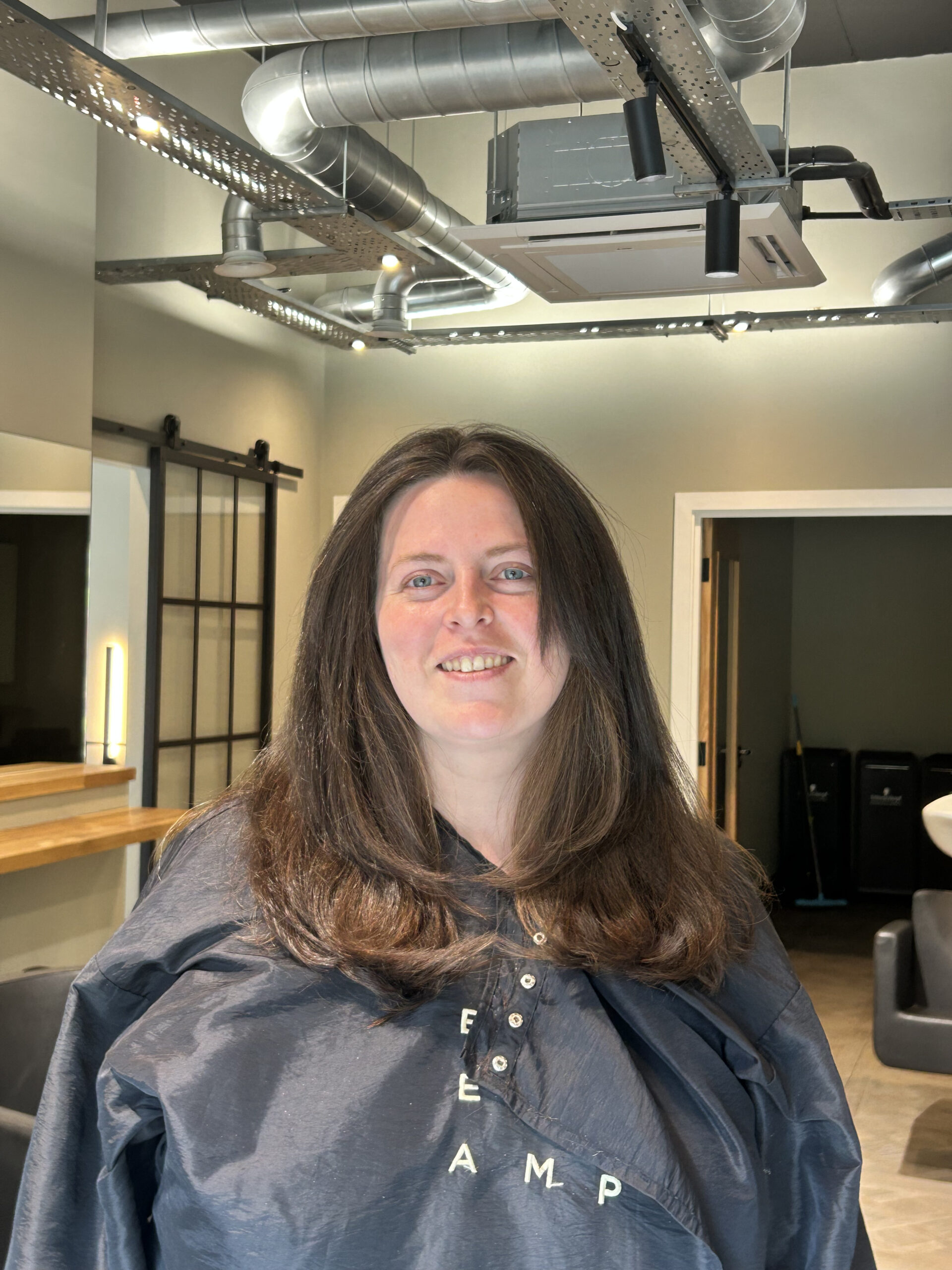 Smiling client with long, glossy brunette hair after a cut and blow dry